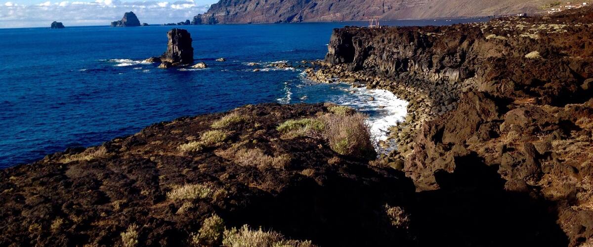 A rugged coastline with rocky cliffs, a prominent rock formation in the sea, and a small settlement on the cliff edge.
