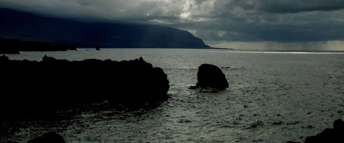 A coastal landscape with rocky outcrops and a cloudy sky.