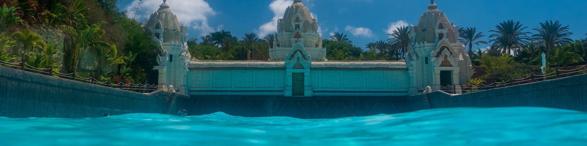 Una piscina azul cristalina con una estructura parecida a un templo al fondo.