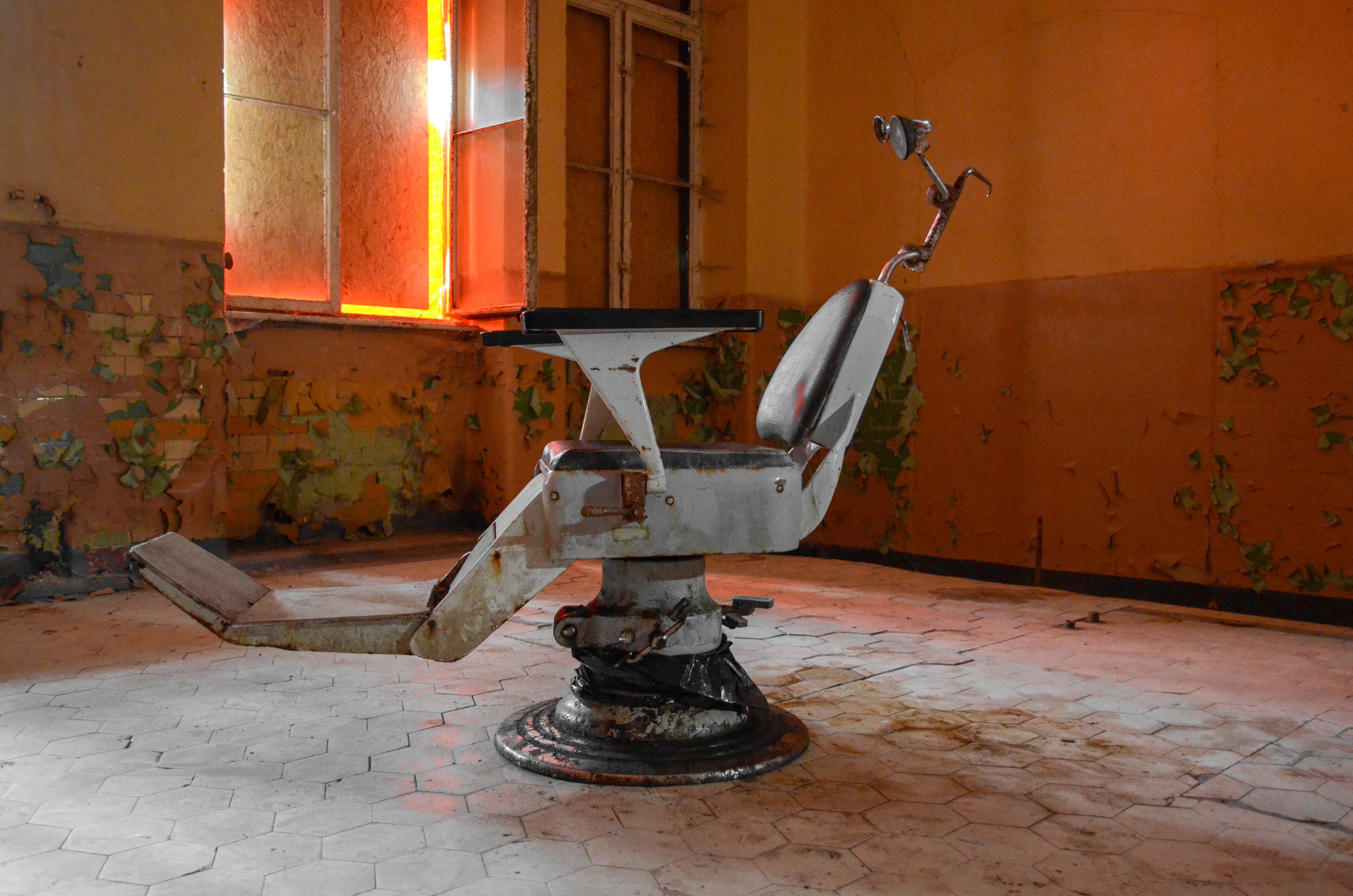 An abandoned barber chair in a dilapidated room with peeling walls and a broken window.