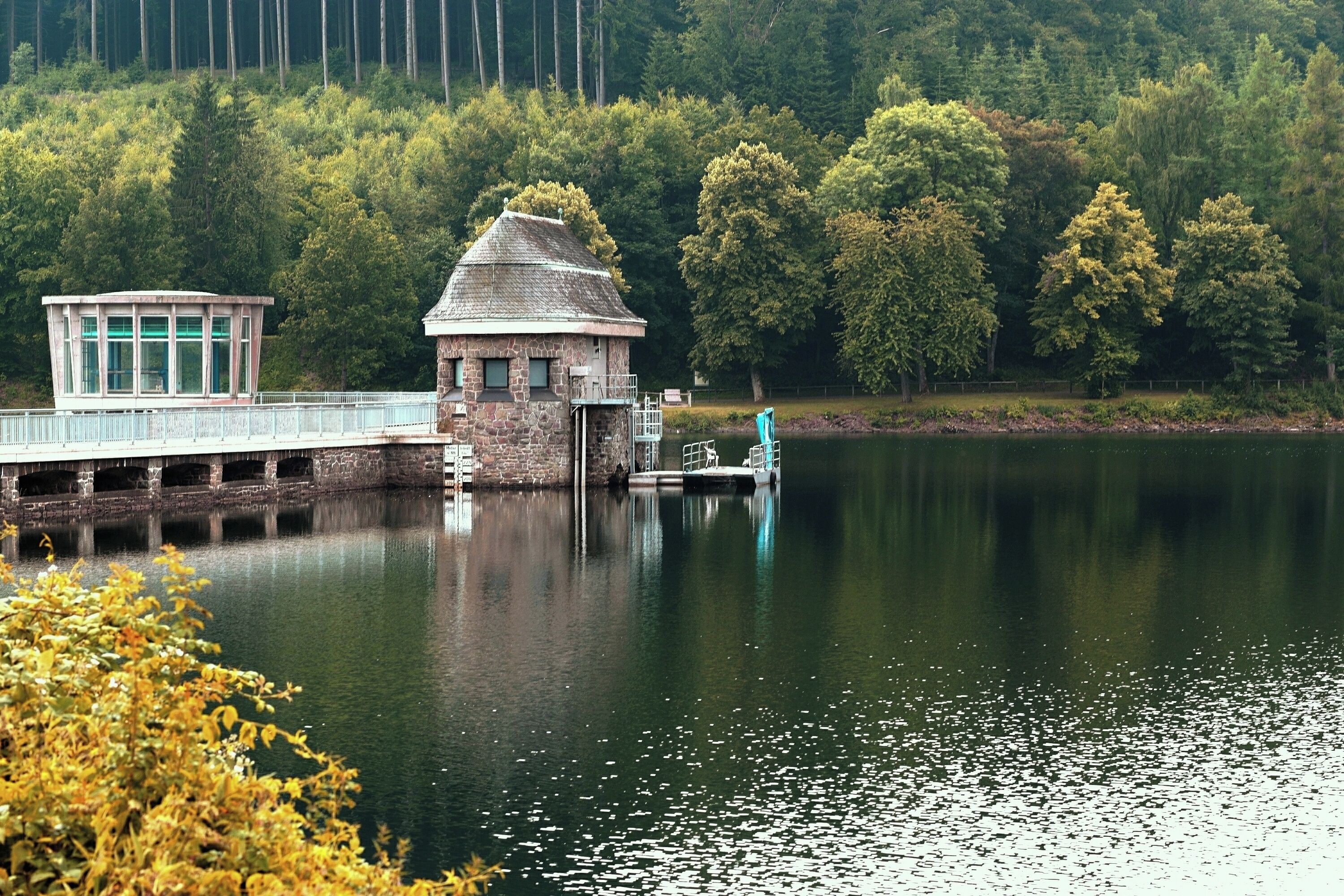 A stone lock house and a bridge over a calm lake, surrounded by dense forest.