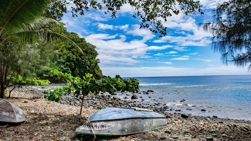 Ocean, beach, trees and small boat in Fagamalo village, American Samoa