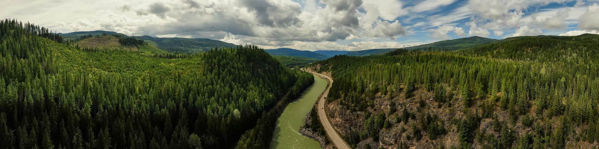 A river winding through a dense forest with a road alongside it and mountains in the background.