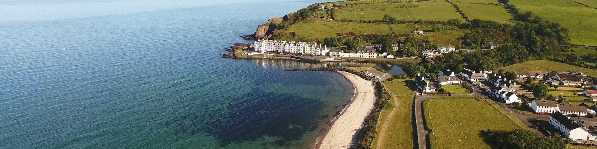 A coastal landscape with a beach, a pier, and a cluster of white buildings.