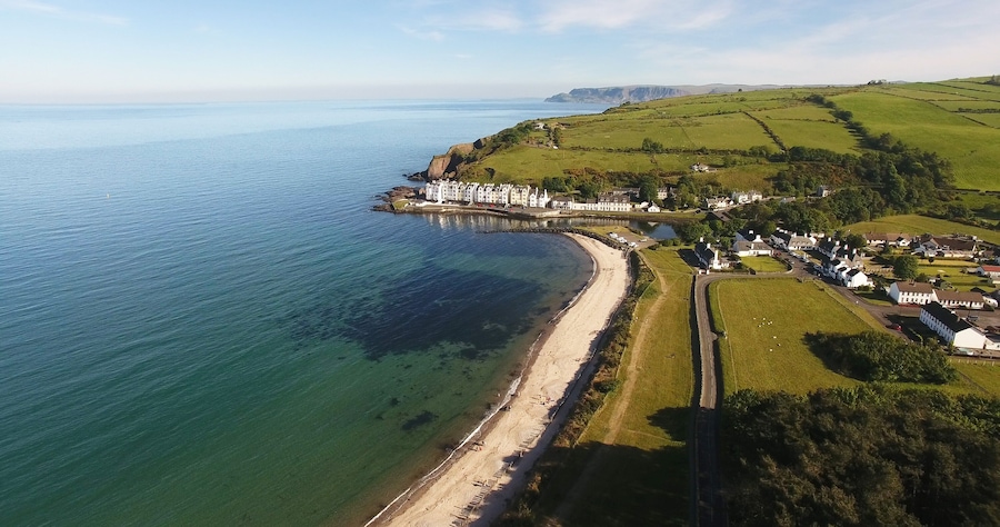 A coastal landscape with a beach, a pier, and a cluster of white buildings.
