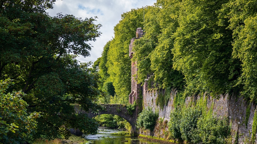Un puente de piedra sobre un río, rodeado de exuberante vegetación y una alta torre de piedra.