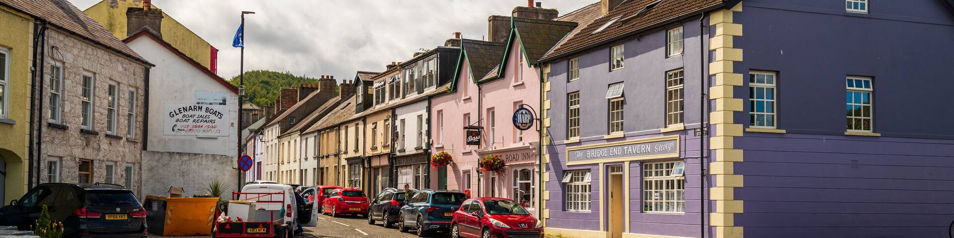 A street lined with colorful buildings, including a purple tavern and a pink building with a sign for 'The Bridge End Tavern'.