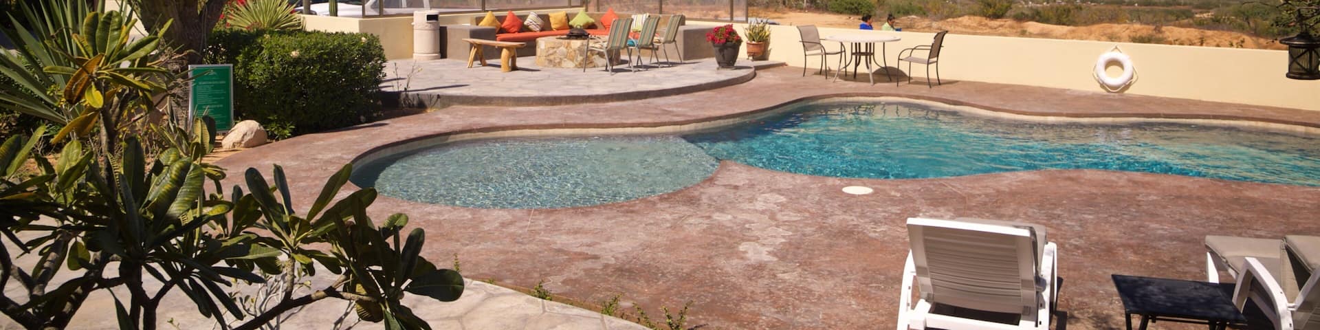 A swimming pool with a view of the ocean, surrounded by outdoor furniture and cacti.