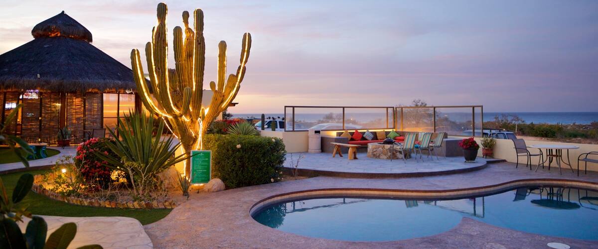 A pool with a cactus, outdoor seating, and a view of the ocean.