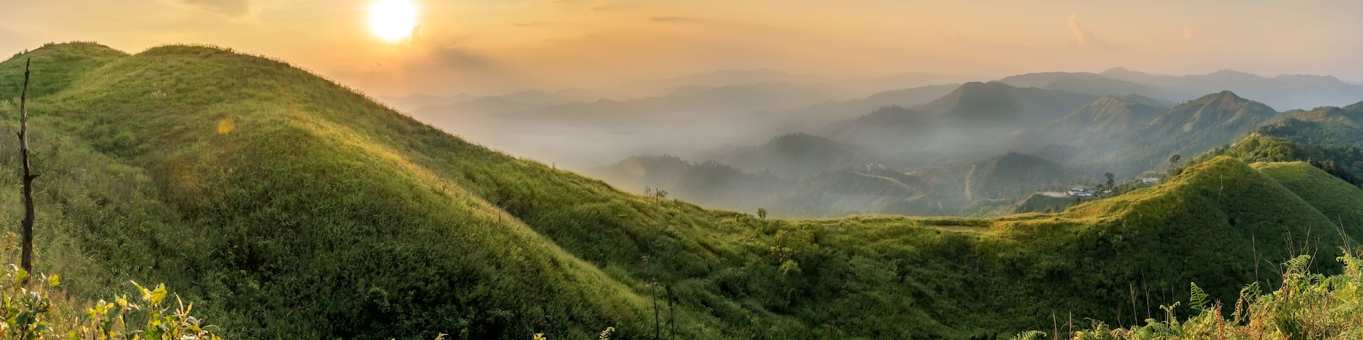 A mountainous landscape with lush green hills and a sun setting in the background.