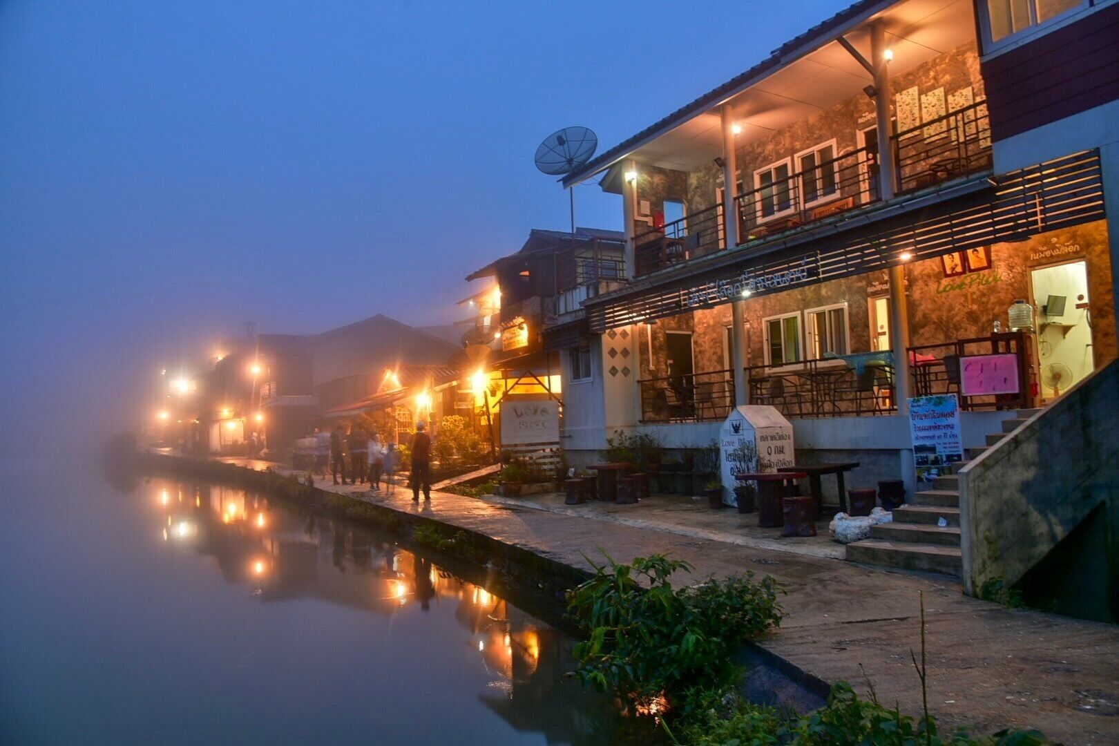 A riverside building with outdoor seating and a satellite dish.