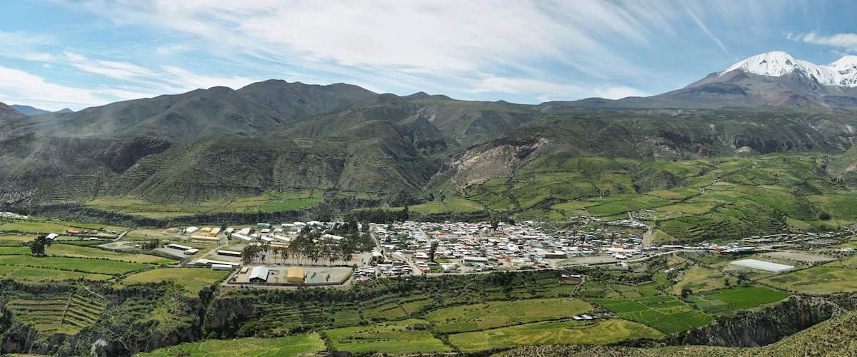 A town nestled in a valley with terraced fields and a snow-capped mountain in the background.