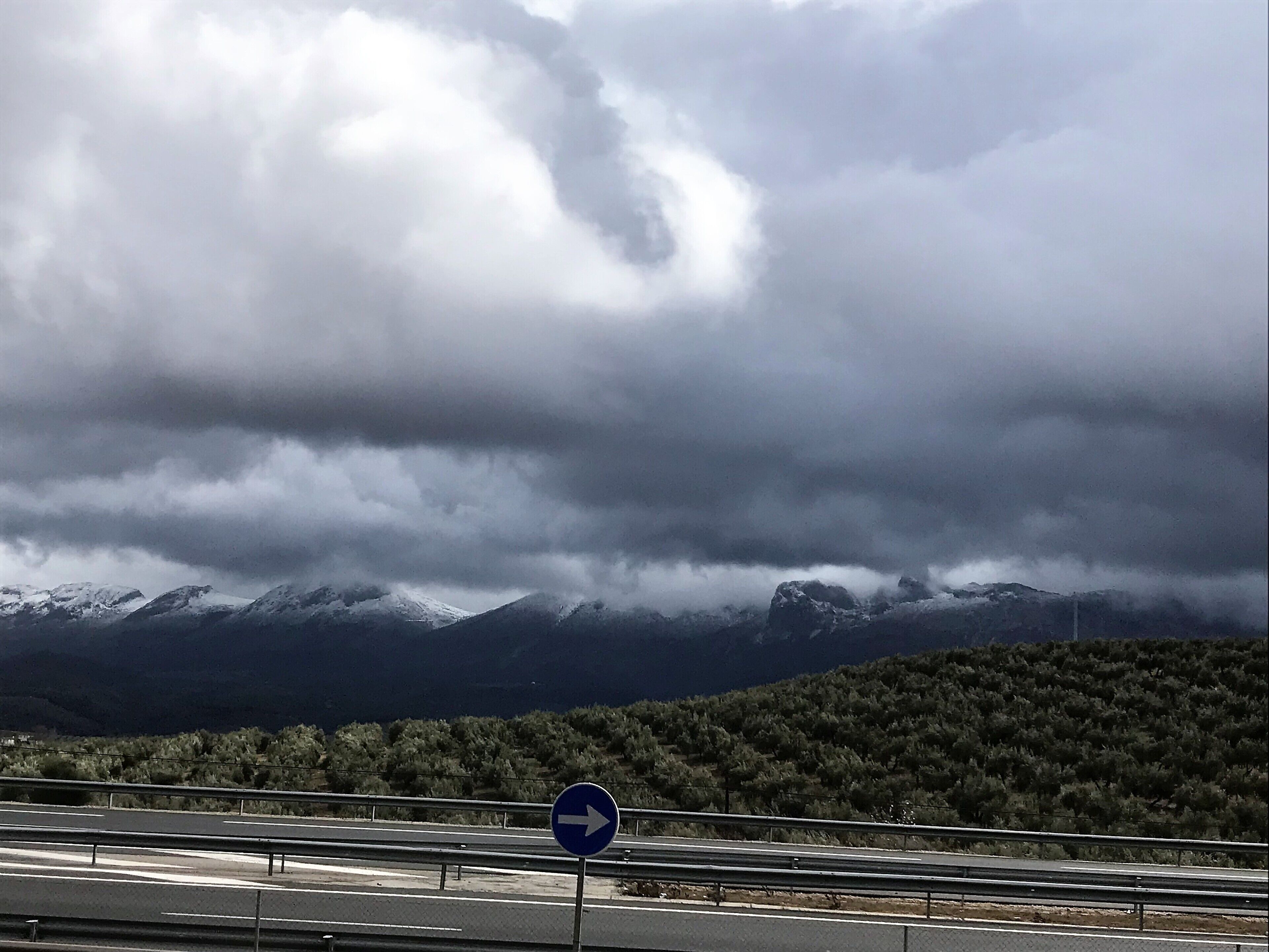 A highway with a blue directional sign and snow-capped mountains in the background.