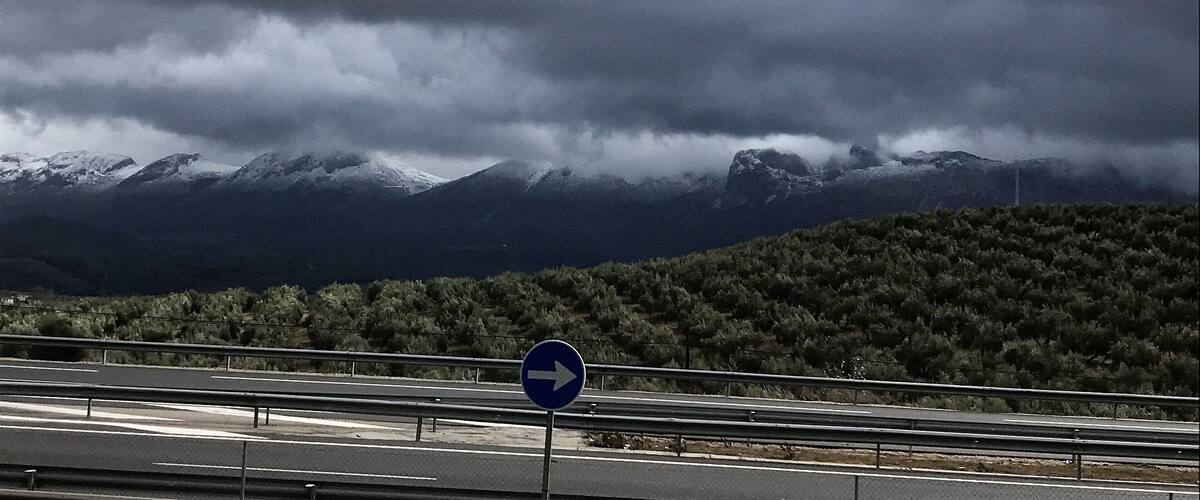 A highway with a blue directional sign and snow-capped mountains in the background.
