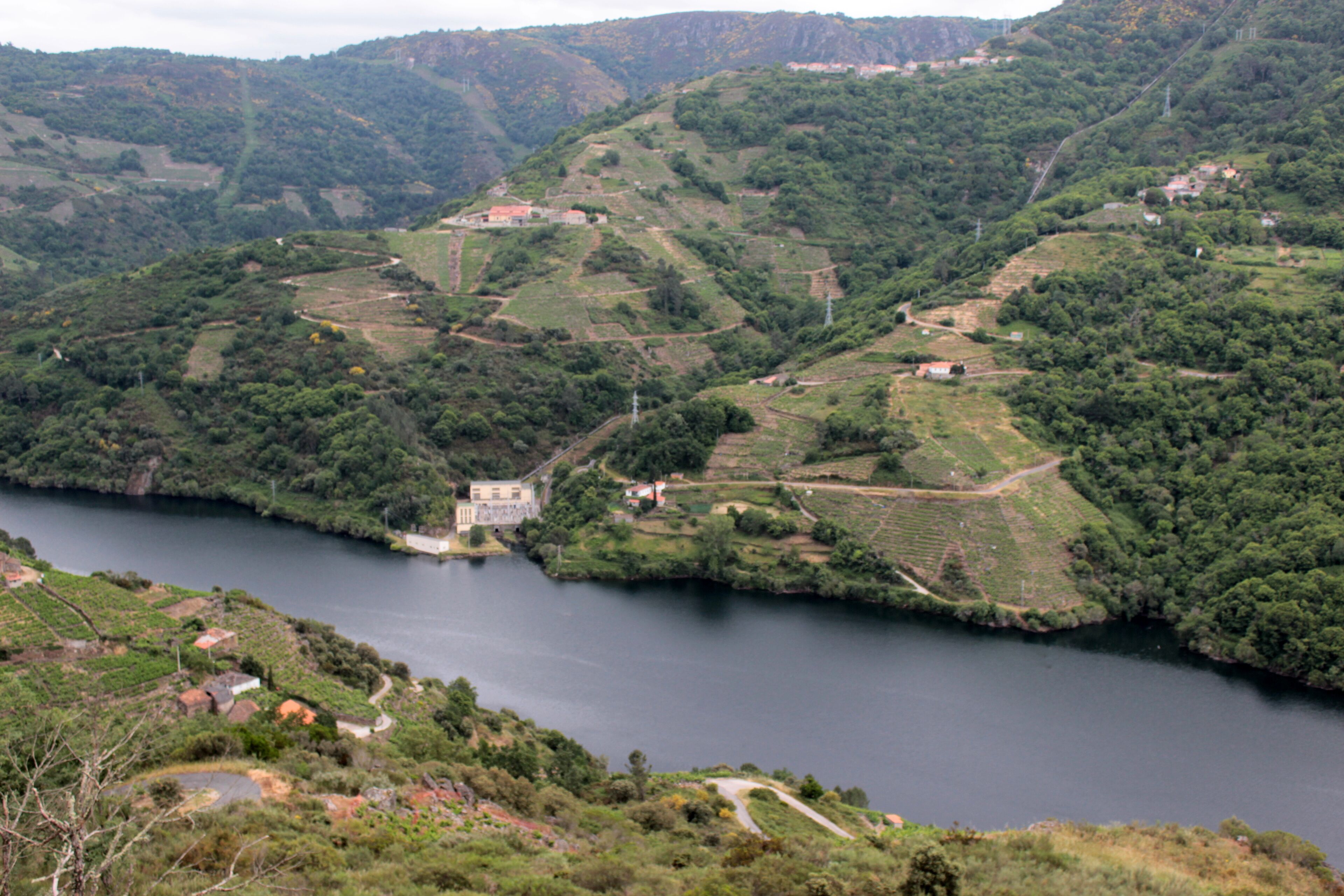 Un río serpentea por un paisaje montañoso salpicado de casas y un edificio destacado cerca del agua.
