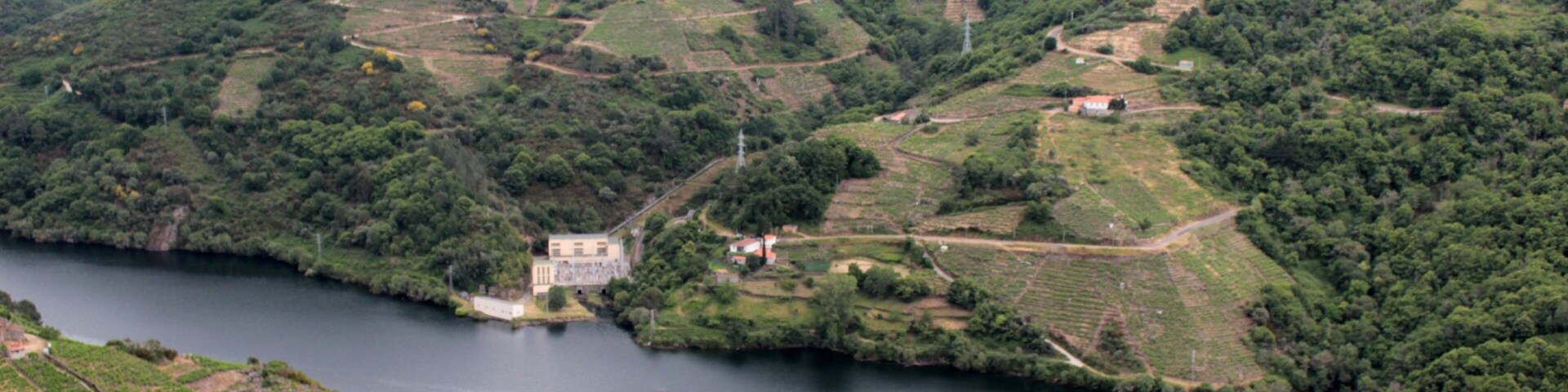 Un río serpentea por un paisaje montañoso salpicado de casas y un edificio destacado cerca del agua.