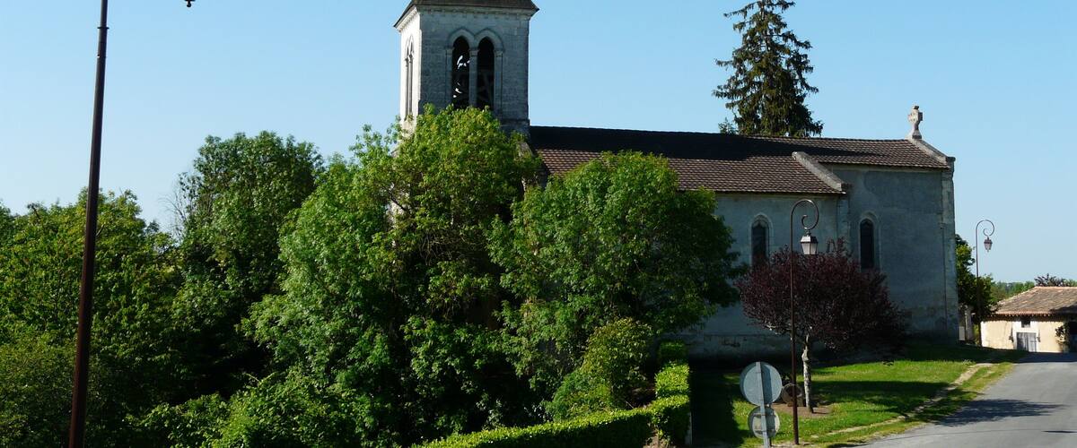 A church with a tall steeple and a bell tower, surrounded by lush green trees and a clear blue sky.