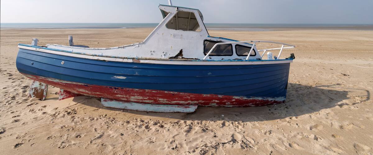 A blue and red boat on a sandy beach with a clear sky.