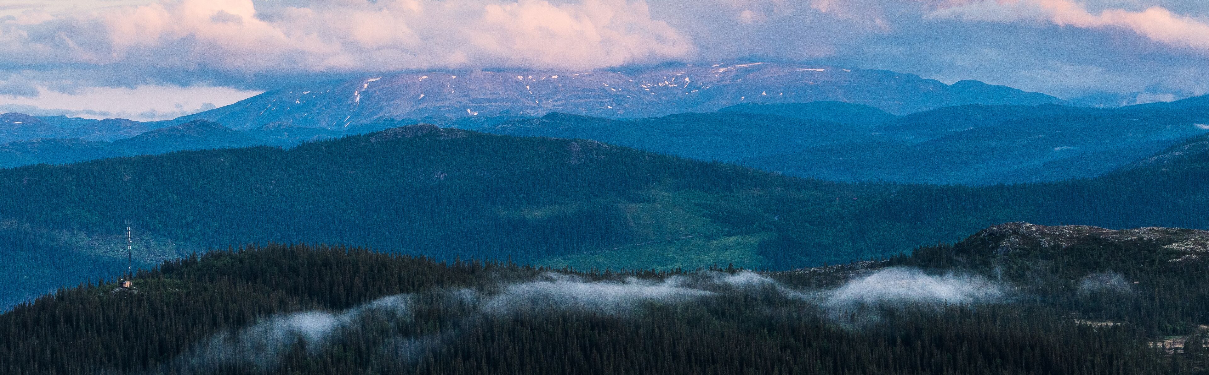 A mountain range with snow-capped peaks and dense forests.