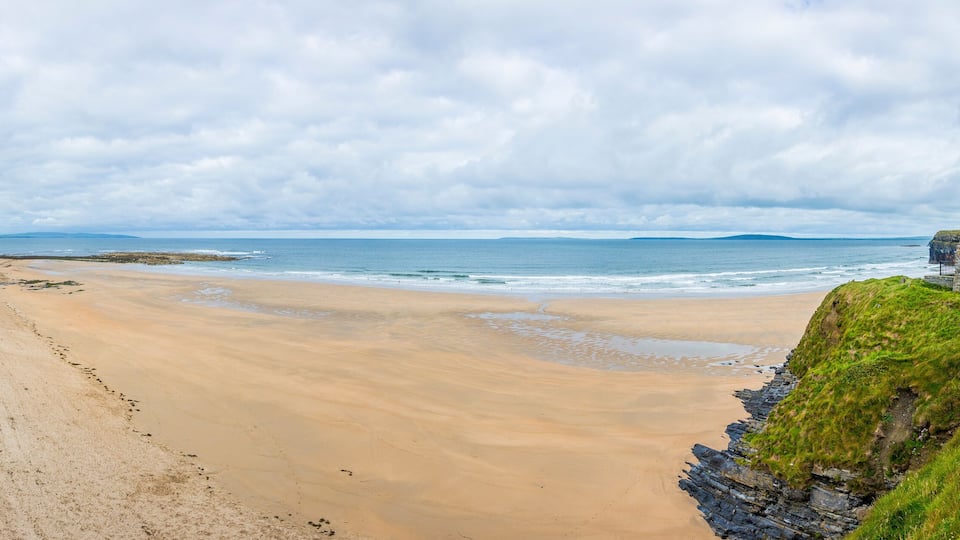 A sandy beach with a stone structure on a grassy cliff.