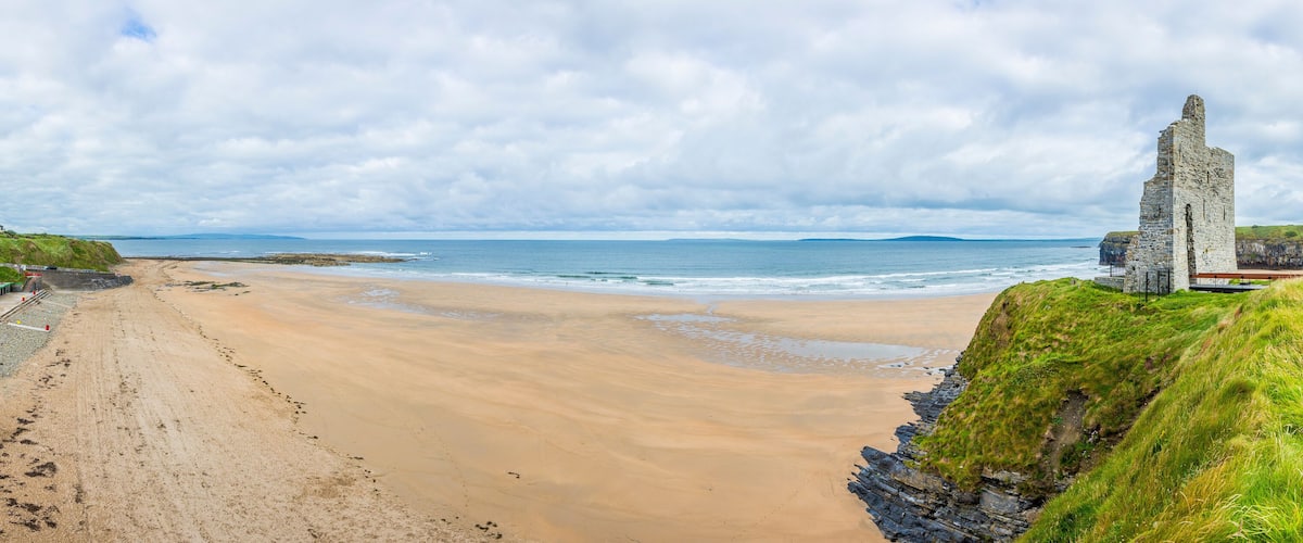A sandy beach with a stone structure on a grassy cliff.