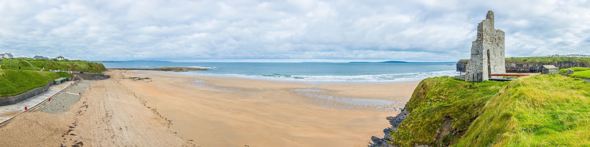 A sandy beach with a stone structure on a grassy cliff.