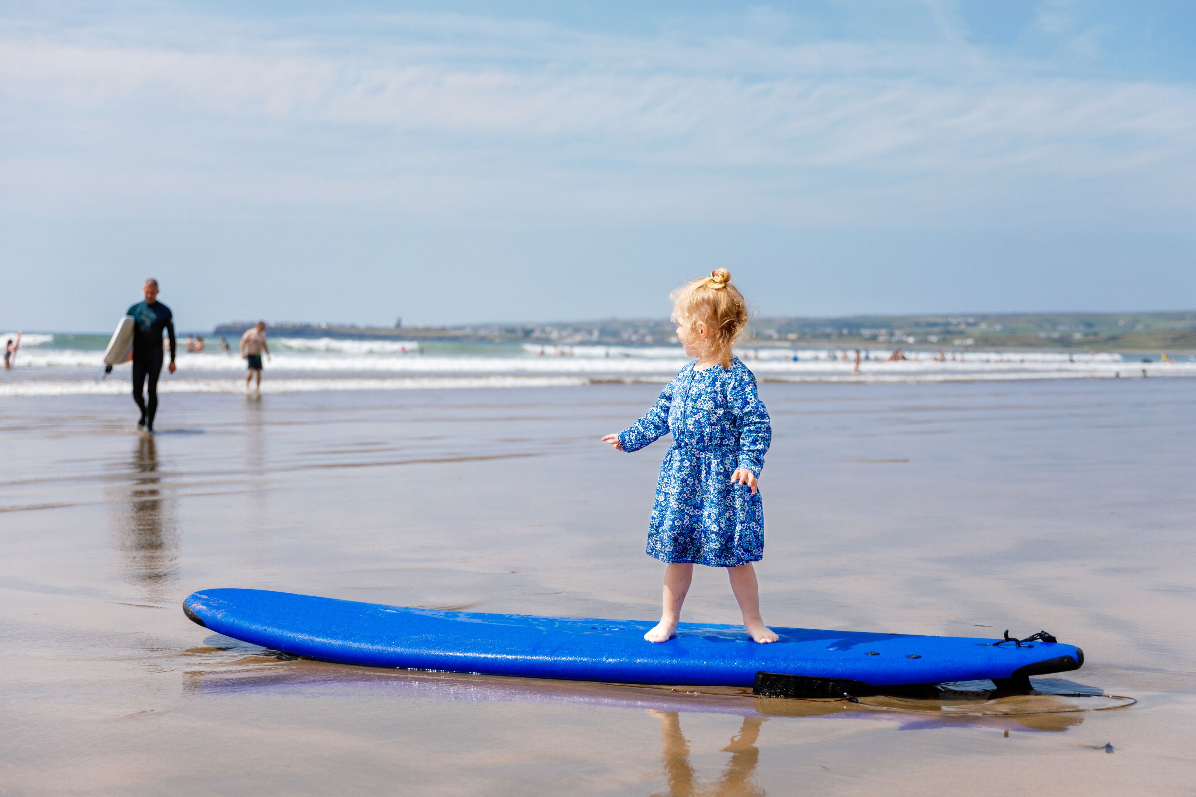 Little cute toddler girl at the Ballybunion surfer beach, having fun on surfboard for the first time, west coast of Ireland. Happy child enjoying Irish summer with family.