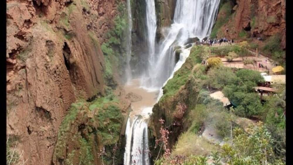 A multi-tiered waterfall surrounded by rugged terrain and sparse vegetation.