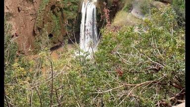 Una cascada escalonada rodeada de terreno accidentado y vegetación escasa.