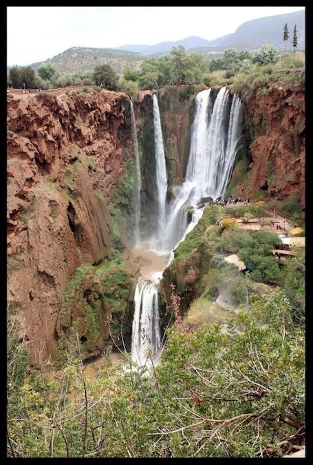 A multi-tiered waterfall surrounded by rugged terrain and sparse vegetation.