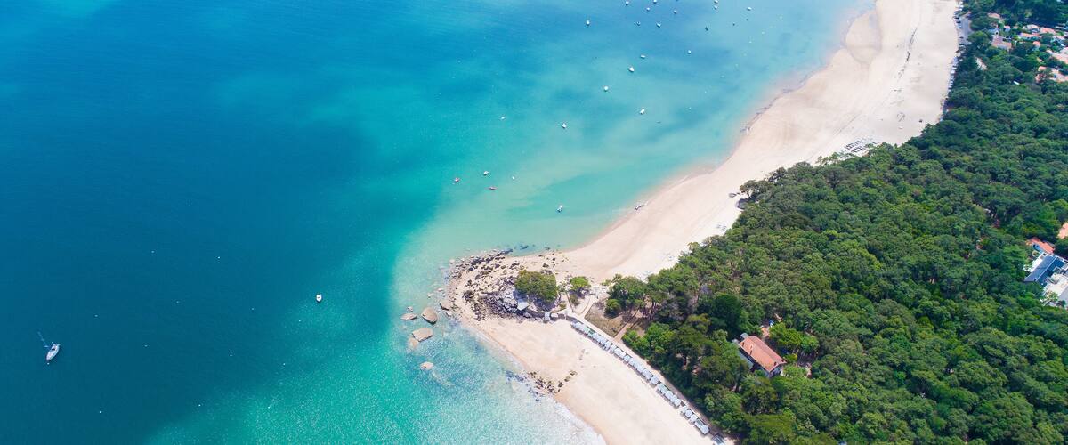 A coastal area with a sandy beach, clear turquoise waters, and dense green forest.