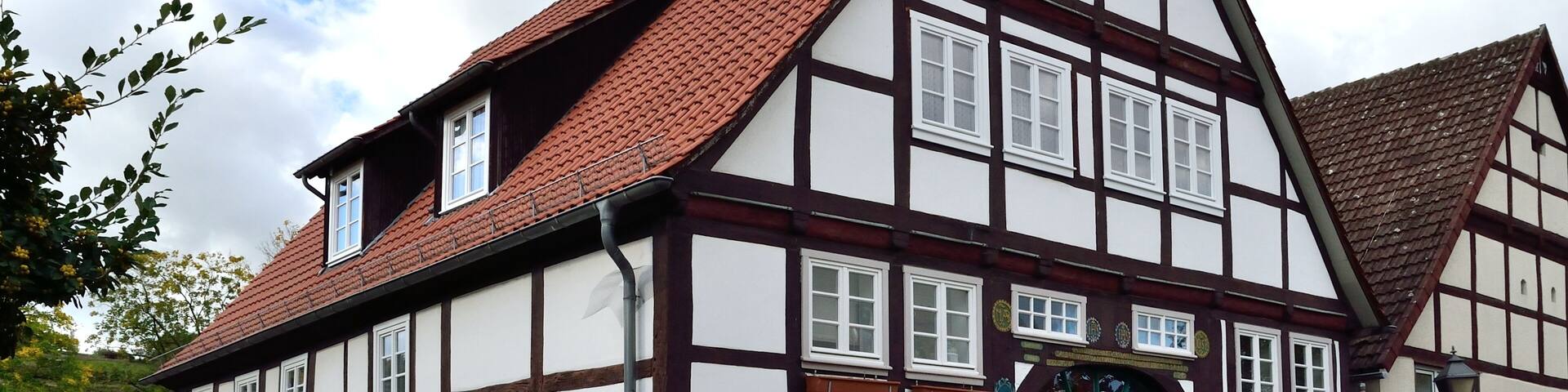 A traditional half-timbered house with a steeply pitched red-tiled roof, white walls, and a green door.