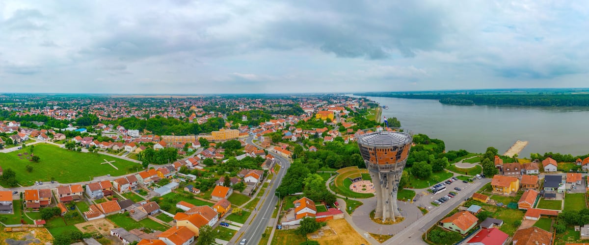 An aerial view of a town with a prominent tower, a river, and surrounding greenery.