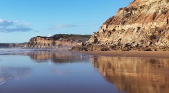 A sandy beach with waves, cliffs, and a clear sky.