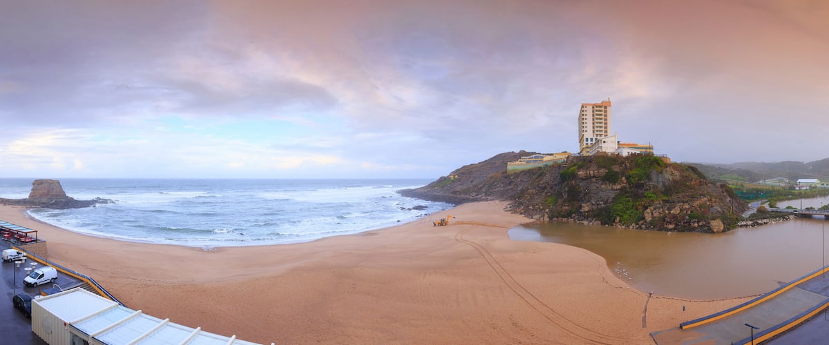 A beach with a construction crane on a small island, a rocky coastline, and a bridge connecting to the mainland.