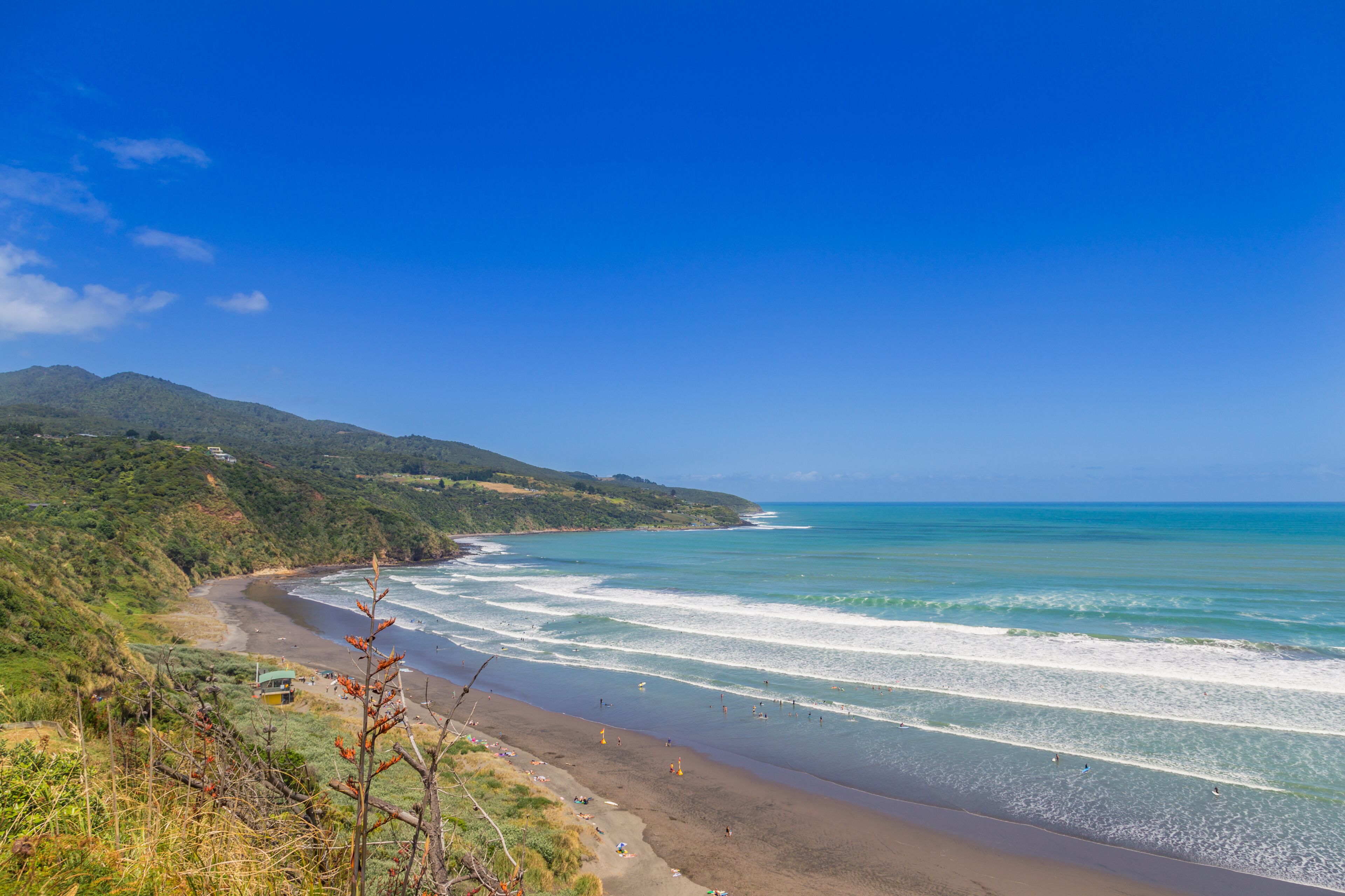 A coastal landscape with a beach, ocean waves, and green hills.