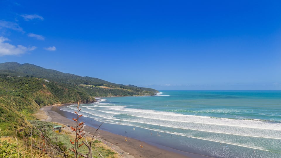 A coastal landscape with a beach, ocean waves, and green hills.