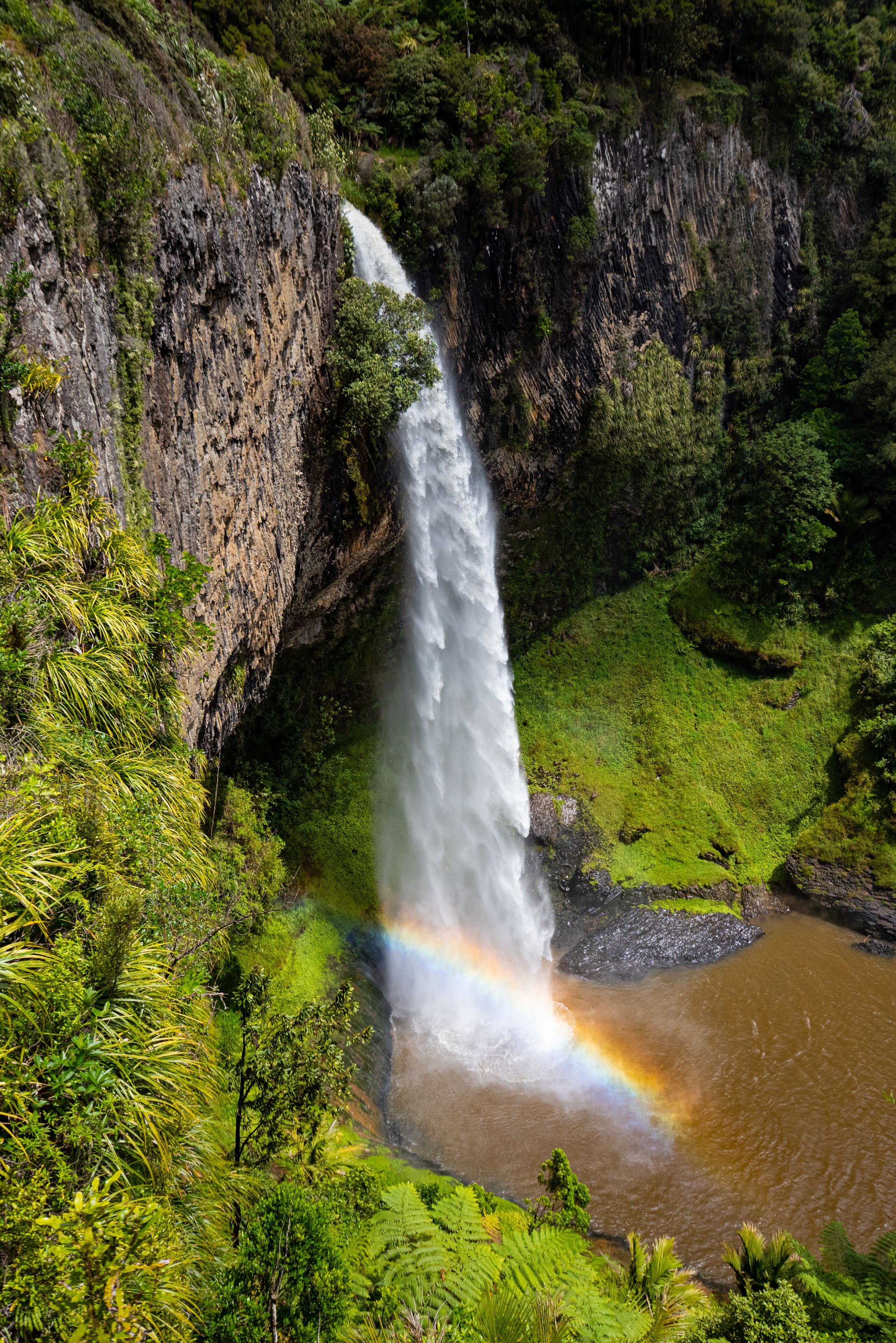 A waterfall cascading down a rocky cliff surrounded by lush greenery.