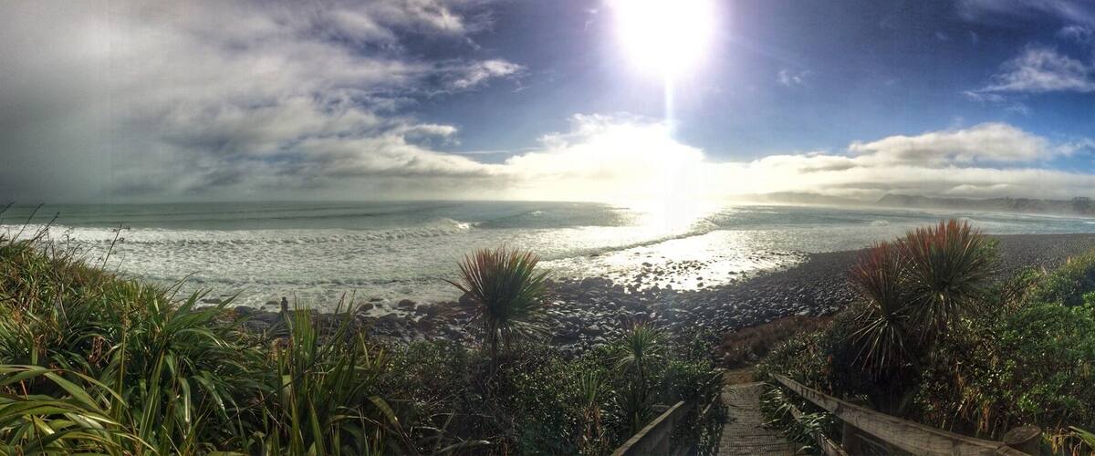 A coastal landscape with a rocky beach, a wooden pathway, and lush vegetation.