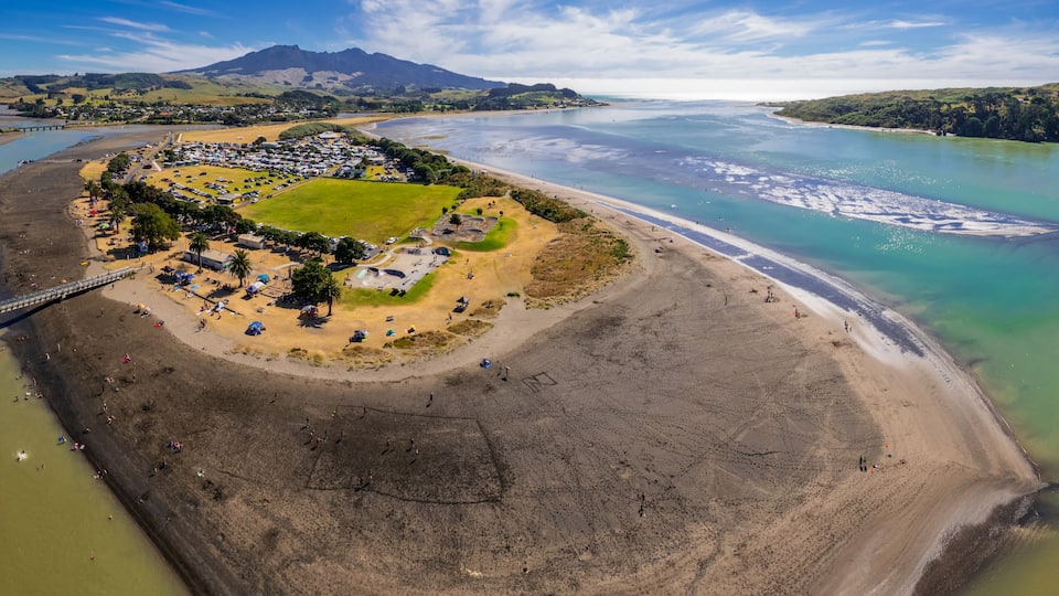 An aerial view of a coastal area with a beach, a bridge, and a mountainous landscape in the background.