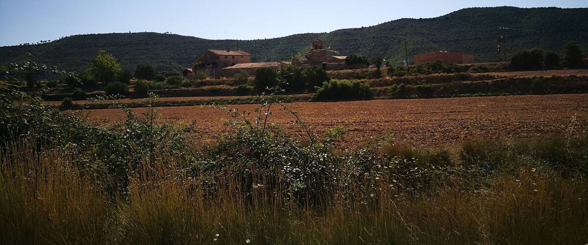 A rural landscape with fields, a hill with scattered buildings, and a clear sky.