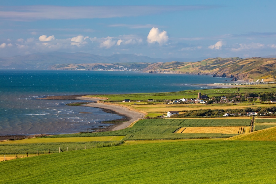 A coastal landscape with green fields, a beach, and distant hills.