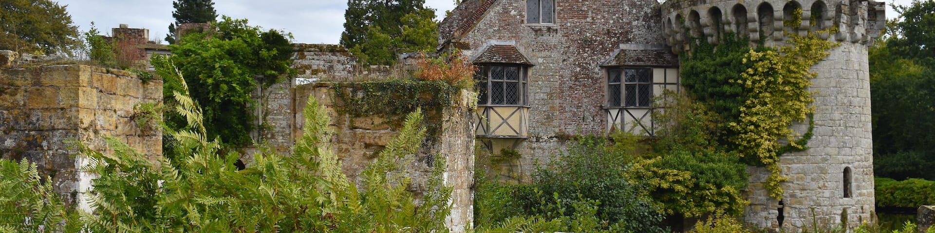 Stone centuries old British medieval castle facade among greenery. It includes residential buildings dominated by great hall for feasting ceremonies place for holding judicial courts and estate office