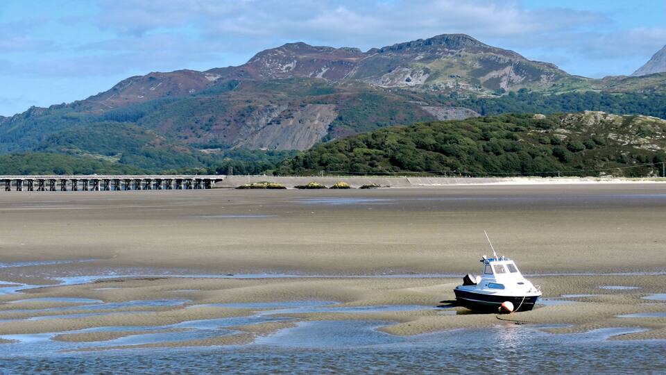 A boat on a tidal flat with mountains in the background.