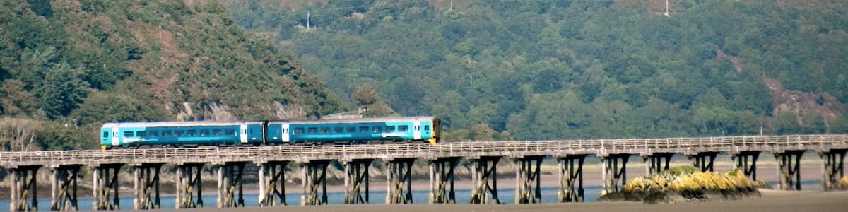 A train on a bridge over water, surrounded by forested hills.