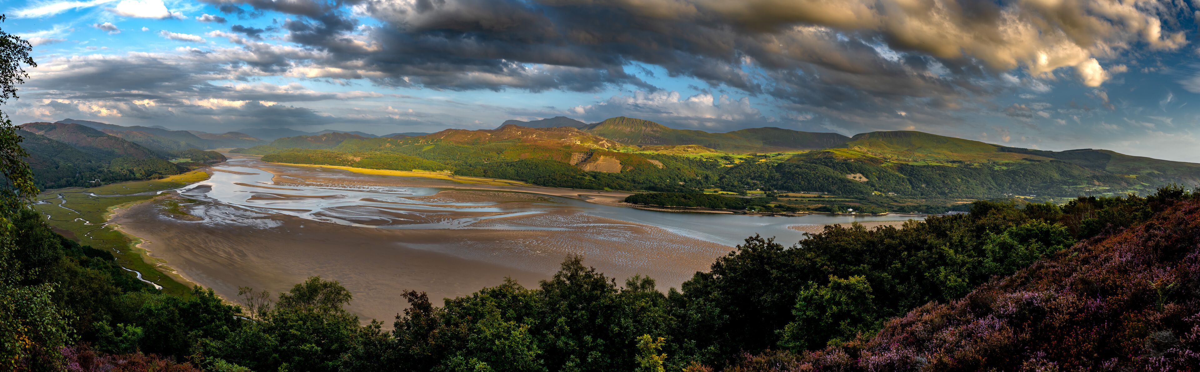A river winding through a valley with mountains in the background and a cloudy sky.