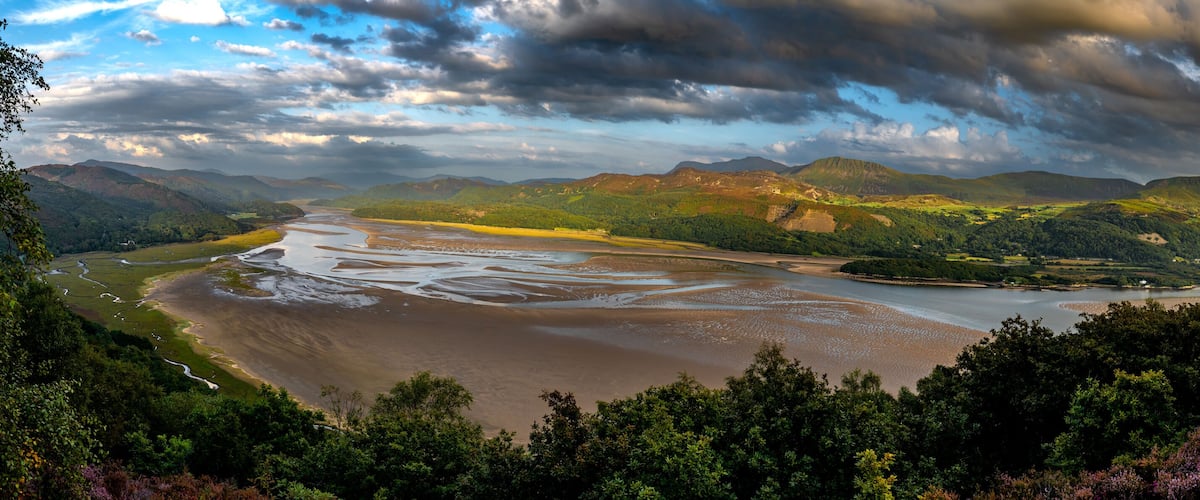 A river winding through a valley with mountains in the background and a cloudy sky.
