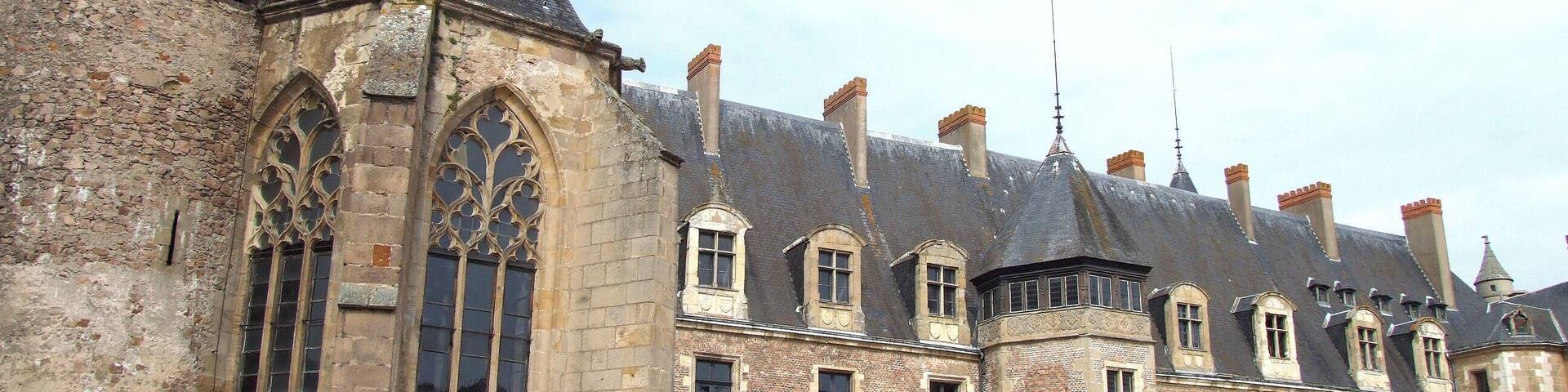 A historic building with a large arched window and multiple chimneys.