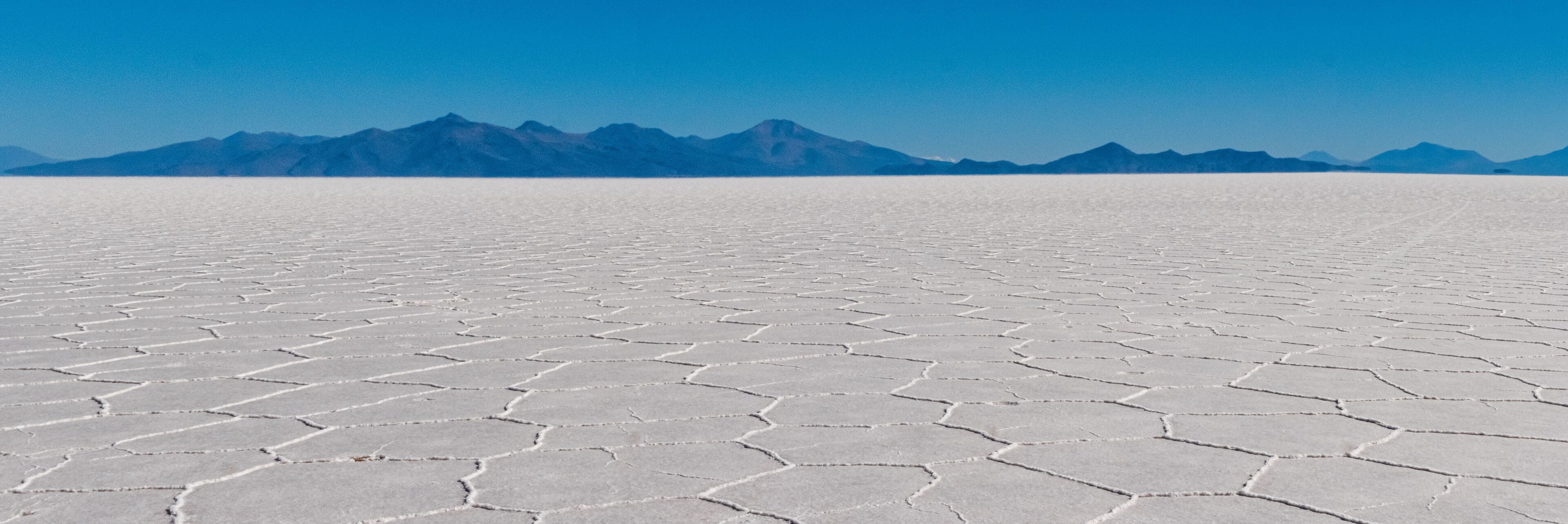 A vast salt flat with hexagonal patterns under a clear blue sky.