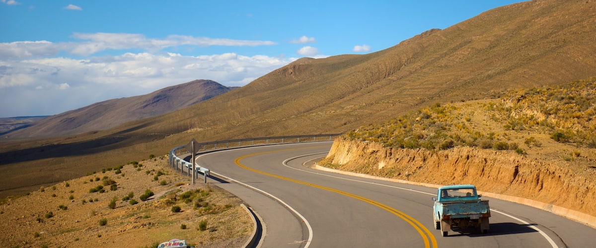 A winding road through a desert landscape with mountains in the background.